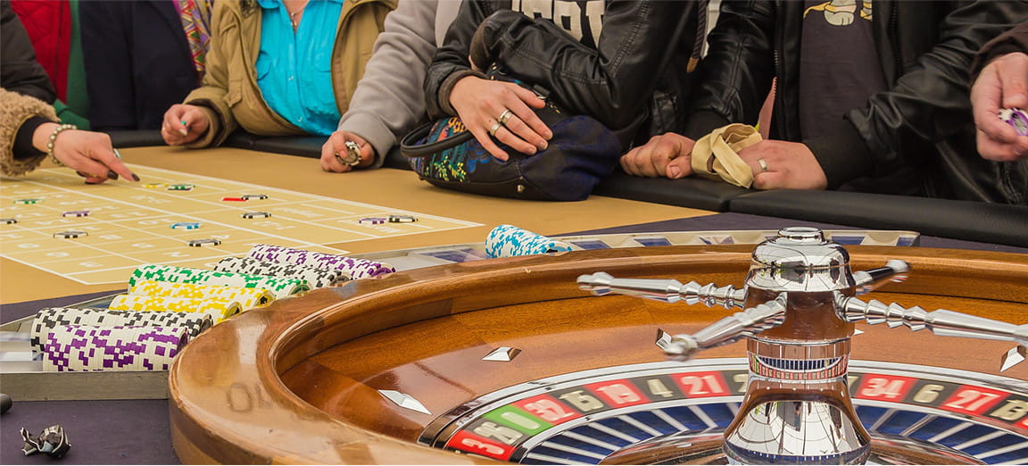 Mesa de ruleta en casino físico con fichas y manos de gente jugando